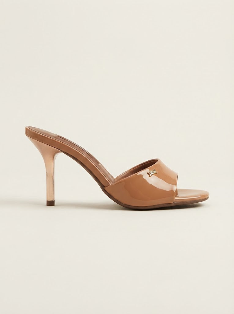 A single nude patent leather mule sandal with a stiletto heel and a small gold logo charm, shown from a side profile on a light beige background.