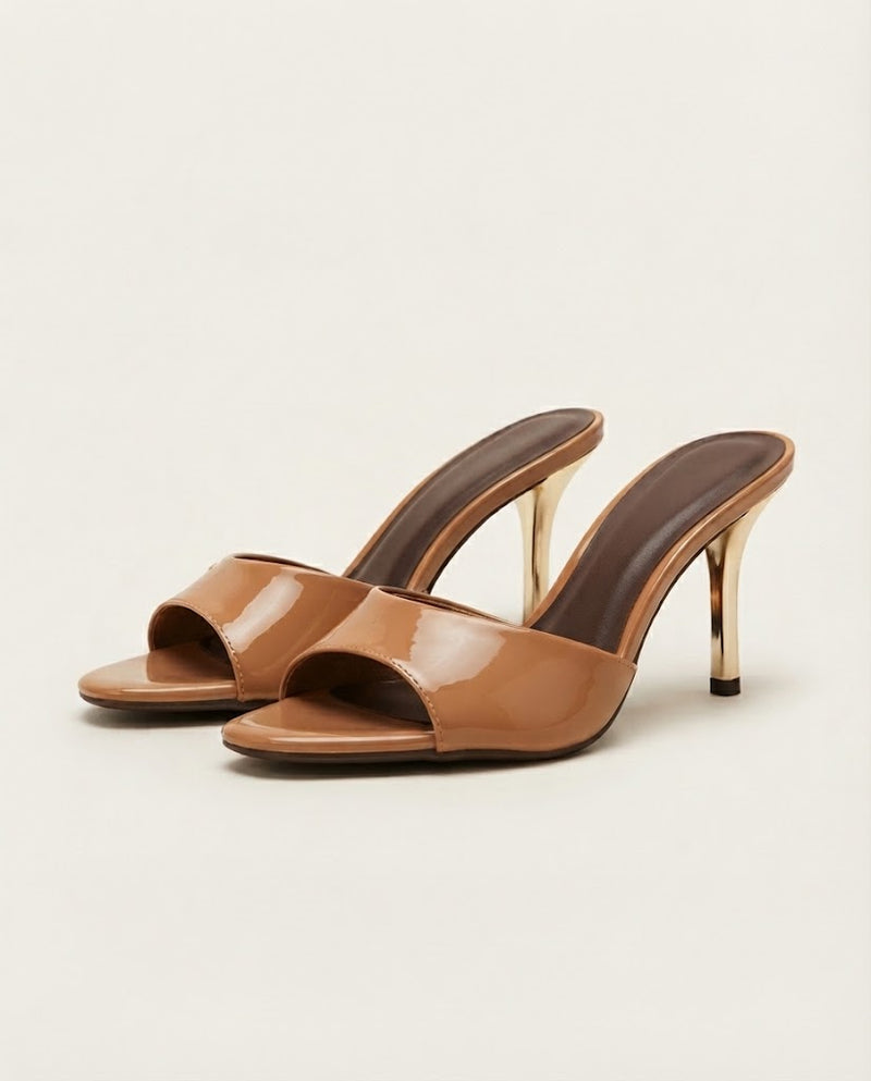 A pair of women's open-toe mule heels in glossy tan patent leather with slim metallic gold stiletto heels, shown on a light beige background.