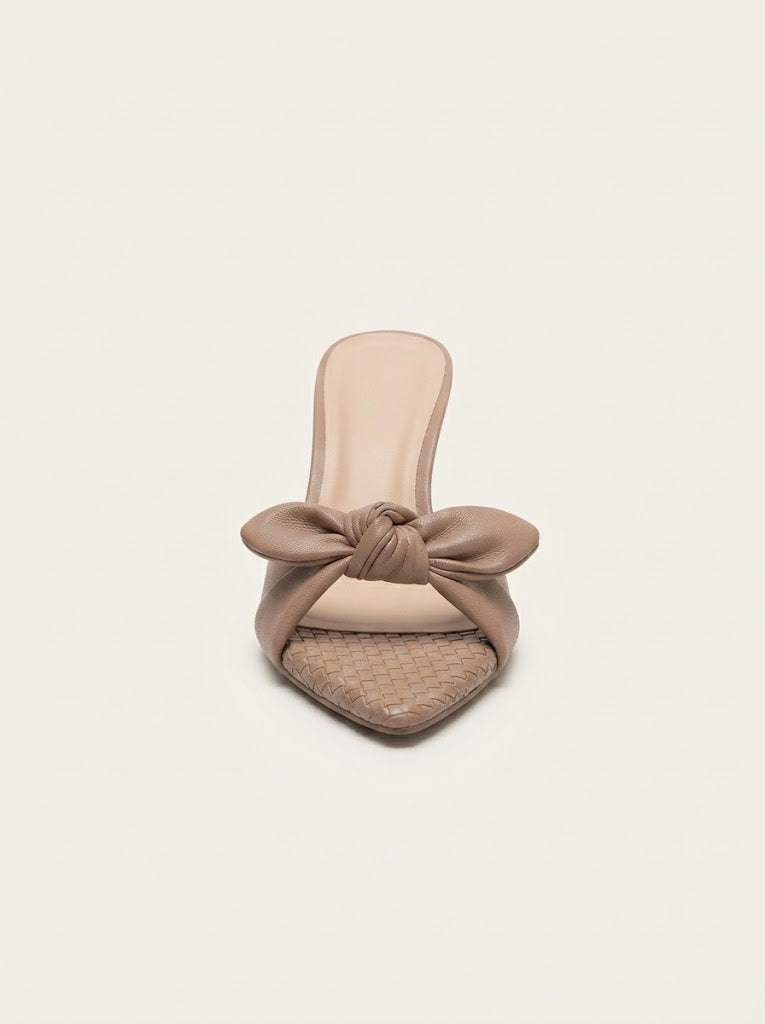 A single taupe-brown leather slide sandal with a knotted bow detail across the instep and a textured woven toe bed, shown against a solid off-white background.