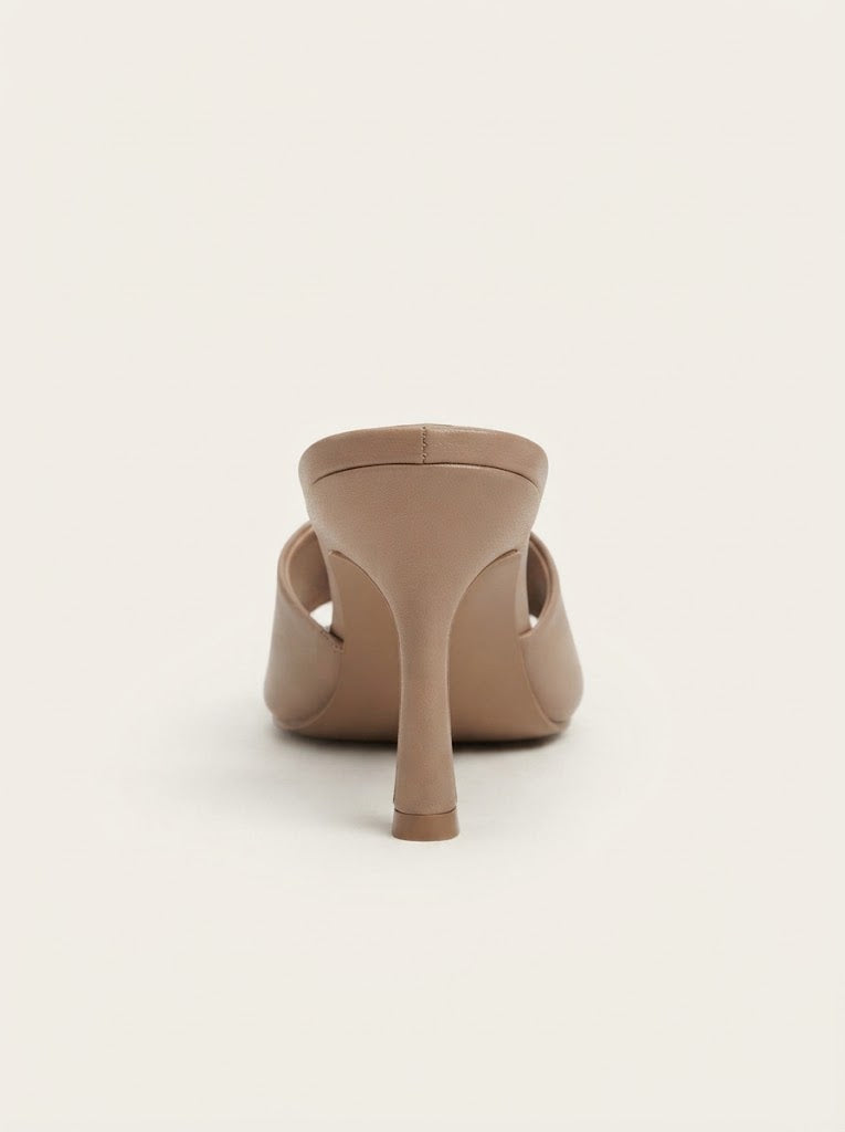 A single beige stiletto mule shoe shown from the back against a solid off-white background.