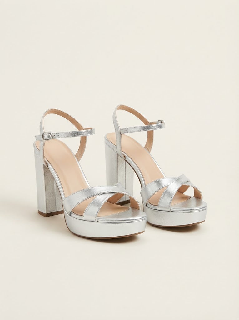 A pair of metallic silver platform sandals with block heels, ankle straps, and open-toe straps, shown on a plain beige background.