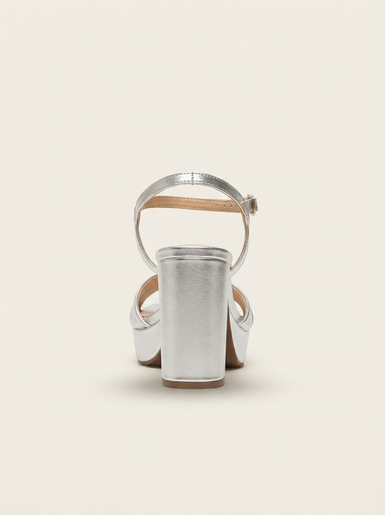 A metallic silver block-heel sandal with an ankle strap, shown from a rear three-quarter view against a solid off-white background.