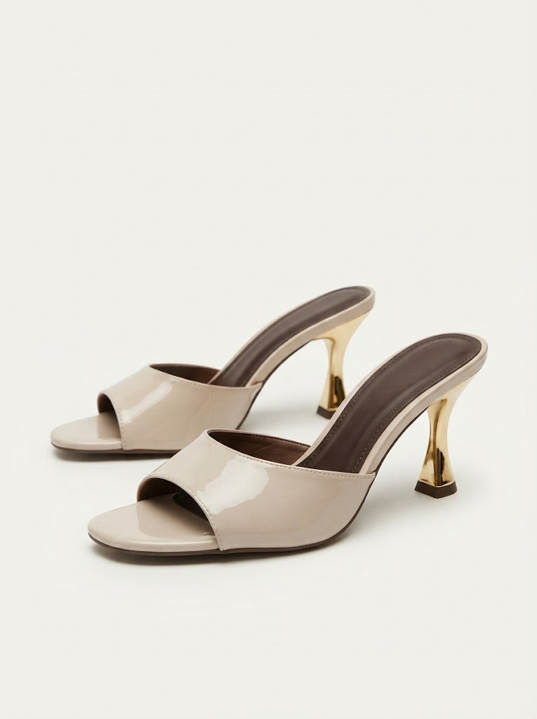 A pair of beige patent leather mule sandals with open toes and distinctive gold-tone high heels, shown on a light off-white background.