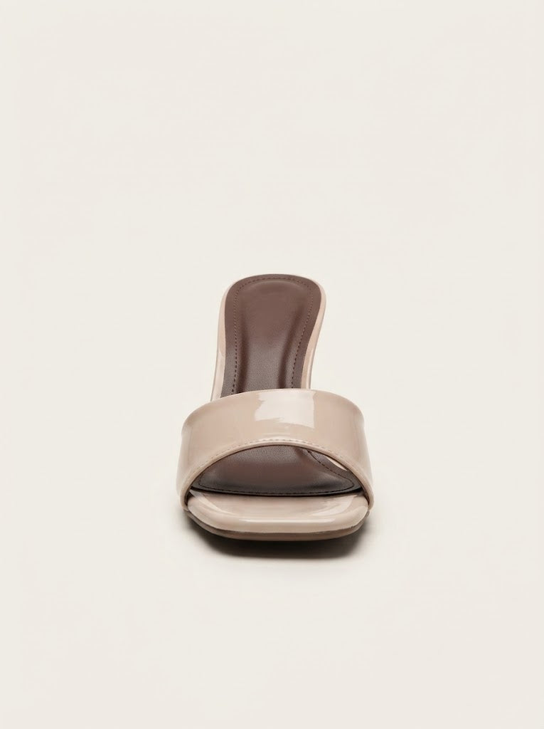 A single women's slide heel sandal in a glossy beige patent leather, featuring a low block heel and a dark brown insole, shown from the front on a light cream background.