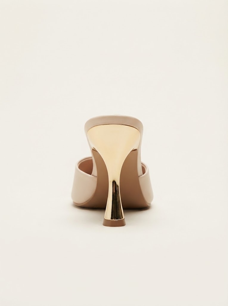 A single nude beige leather mule high heel shown from the back, featuring a metallic gold accent on the heel and a matching gold-toned insole, set against a plain off-white background.