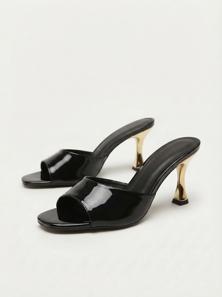 A pair of black patent leather mule sandals with open toes and sculptural gold-tone high heels, shown on a clean white background.