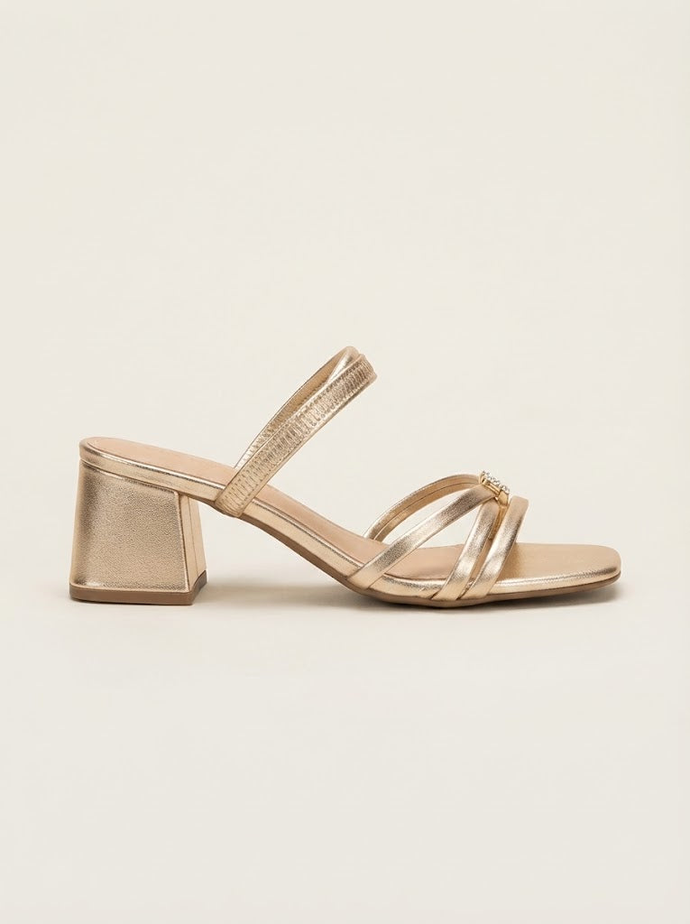 A single metallic gold block-heel sandal with thin strappy details across the instep and a slim ankle strap, shown in profile against a solid off-white background.