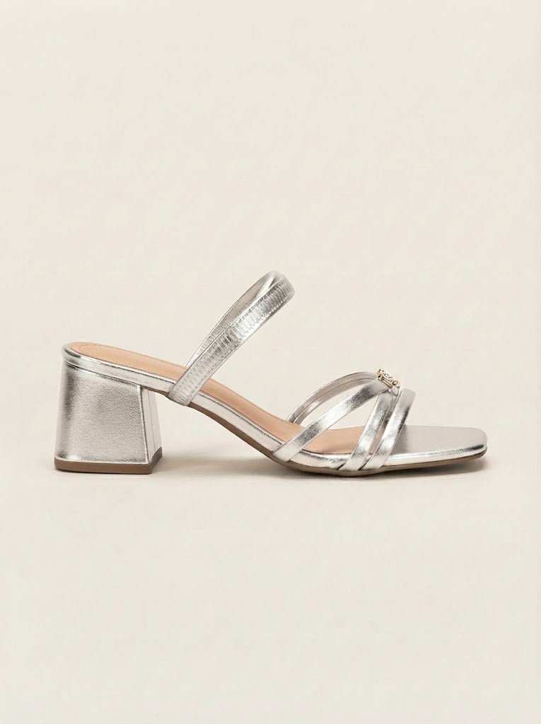 A single metallic silver heeled sandal with a block heel, square toe, and thin strappy design with a small gold buckle detail, shown against a plain beige background.