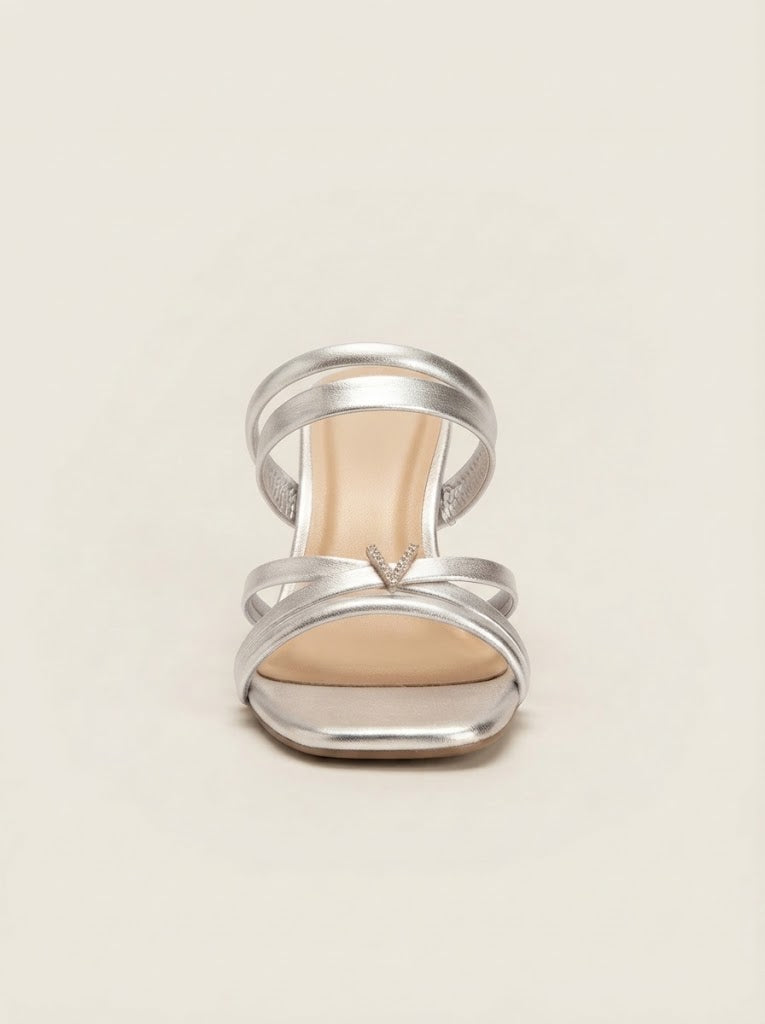 A single metallic silver strappy sandal with a low block heel and a small rhinestone detail on the front strap, shown from a top-down view on a light beige background.