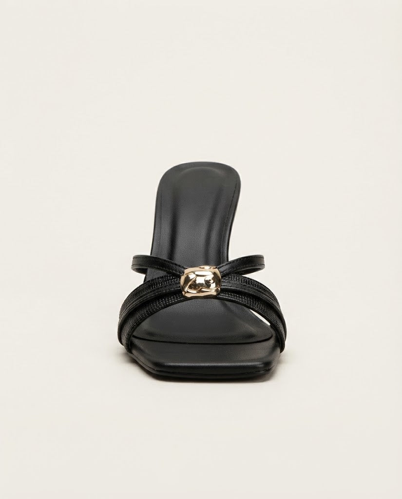 A single black heeled sandal with a square toe, featuring a wide satin strap and a thin strap accented by a gold-tone metal ring, shown against a plain off-white background.