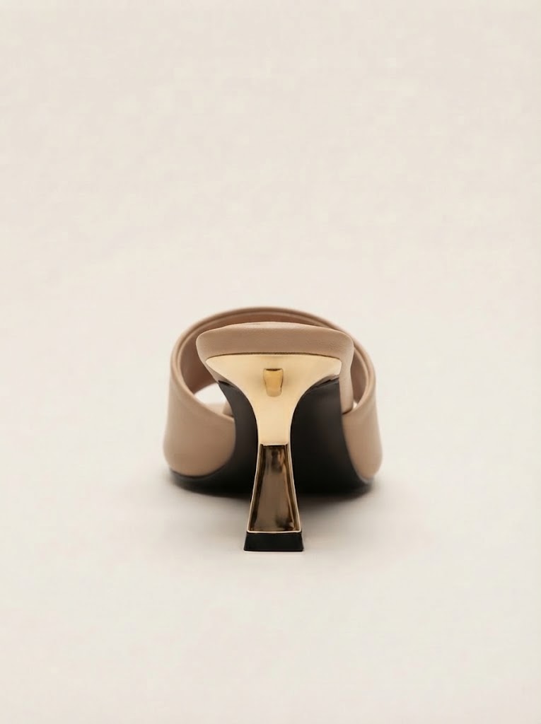 A single beige leather slingback mule with a unique metallic gold and black geometric heel, shown from a rear three-quarter view on a light beige background.