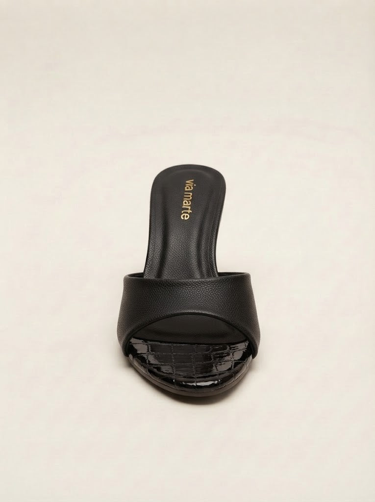 A single black slide sandal with a textured strap and a glossy crocodile-embossed toe cap, shown from the front on a light beige background. The brand name 'valentino' is printed in gold on the insole.
