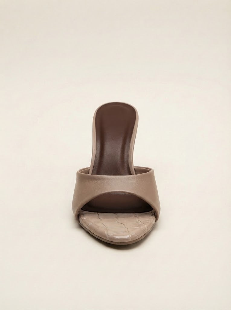 A single taupe slide sandal with a textured crocodile-patterned toe strap and a dark brown heel, shown against a solid cream background.