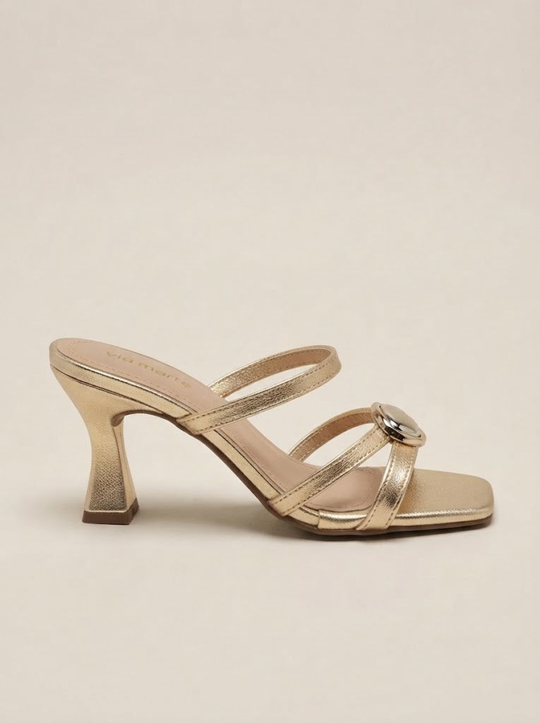 A metallic gold strappy mule sandal with a square toe and a chunky block heel, shown from a side profile on a neutral beige background.