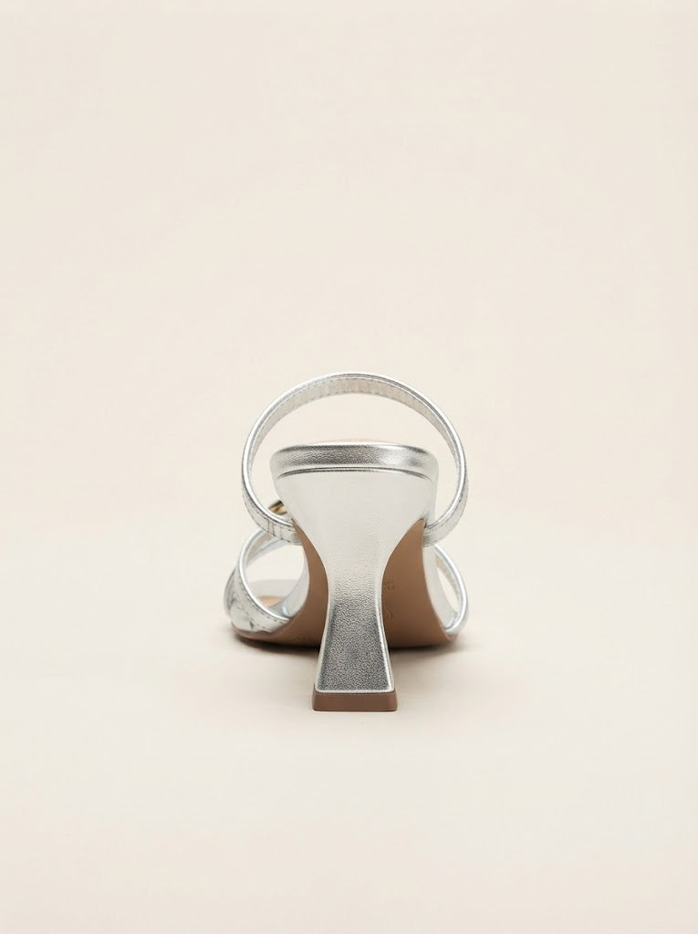 A single metallic silver heeled sandal with a wide loop strap and block heel, shown from the back on a light beige background.